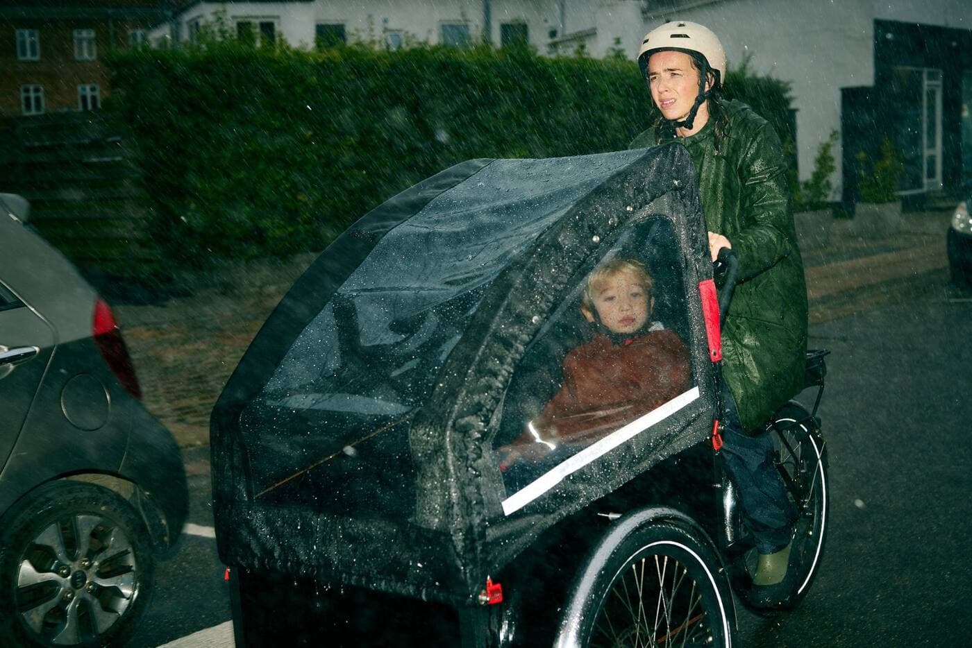 Mor på ladcykel med barn i regnvejr, still fra en produktion for en bankkunde